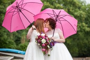 Lesbian couple in wedding dresses kissing under pink umbrellas