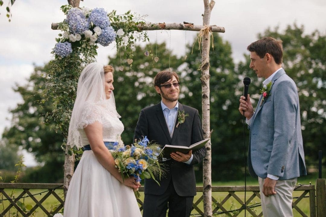 Bride and groom saying vows under a flowery alter at an outdoor wedding