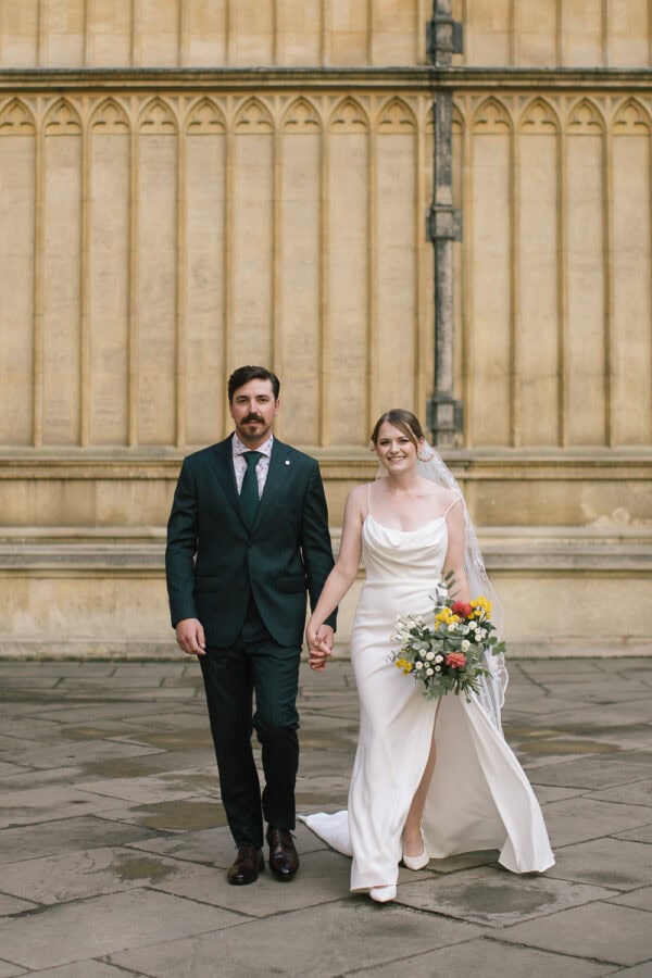 Bride and groom strolling through the historic streets of Oxford, past golden sandstone colleges