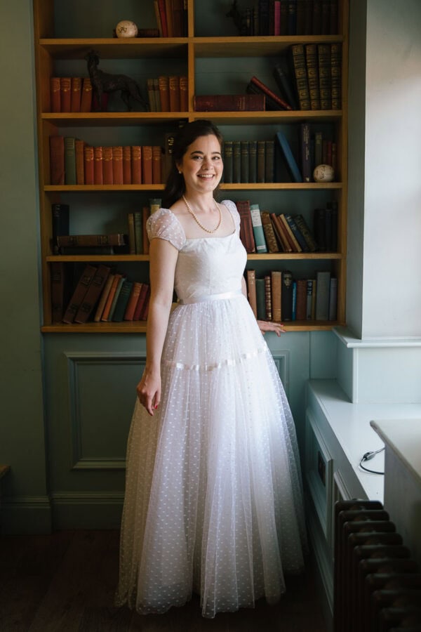 bride standing un front of a traditional bookcase with old books